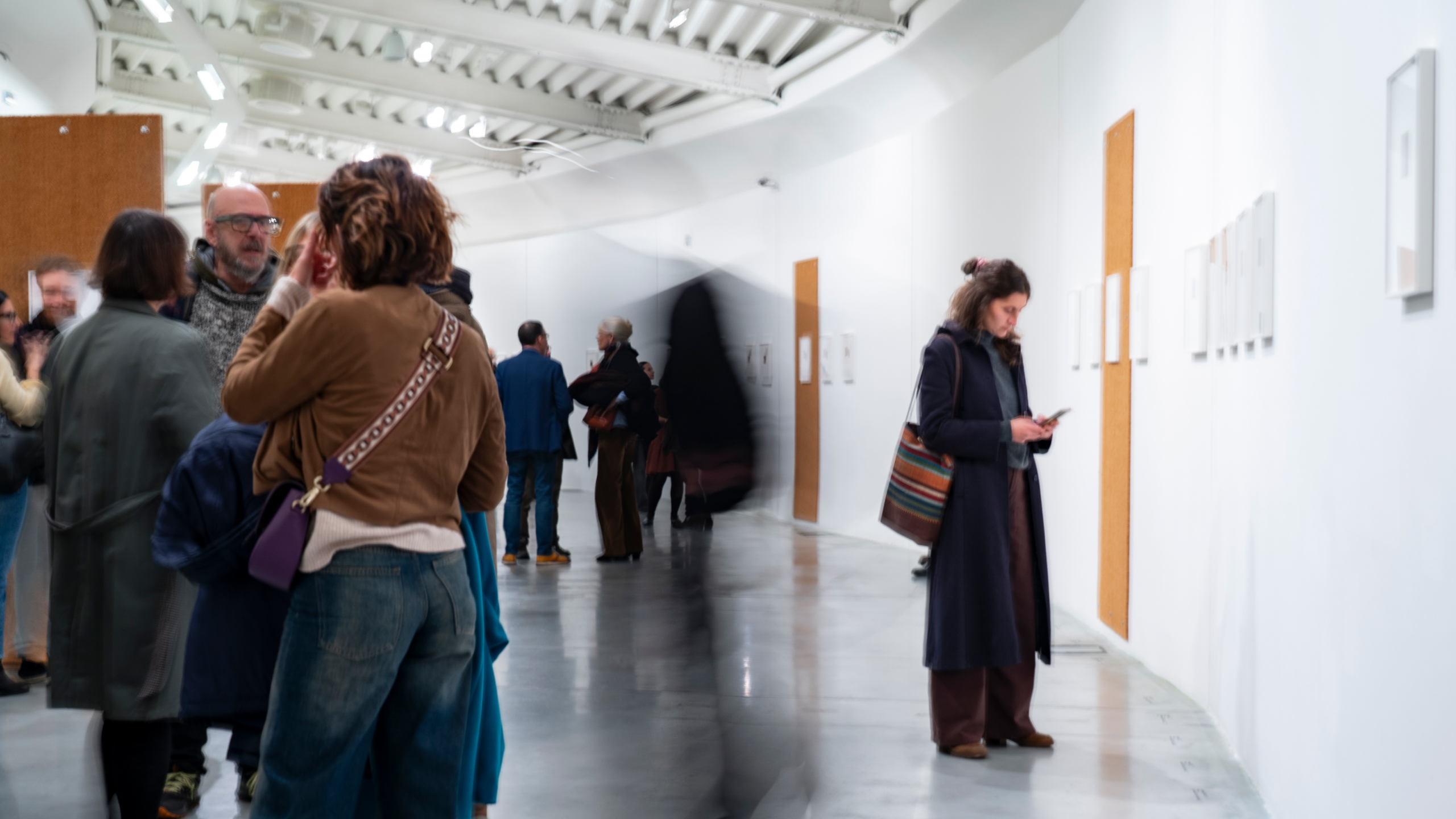 Visitors in a gallery at the Centro Pecci look at artworks on white walls; some people chat while a woman reads the wall labels.